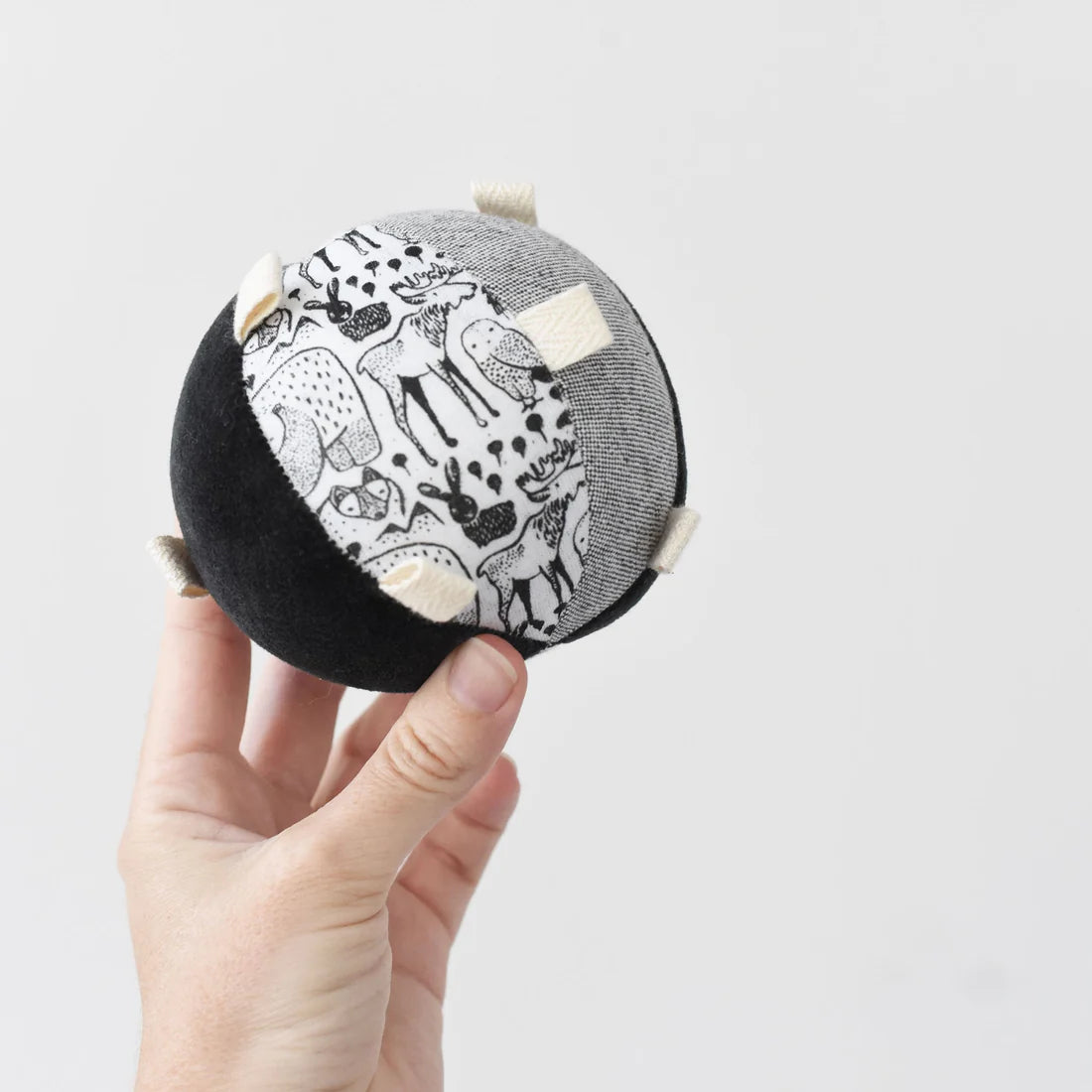 Hand holding the Organic Taggy Ball | Nordic, featuring black and white animal prints with textured tags for sensory play.