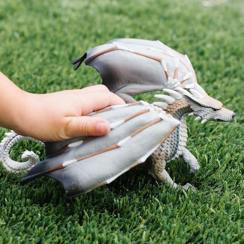 Child holding the Wolf Dragon toy with raised forepaw and large wings on green grass background.