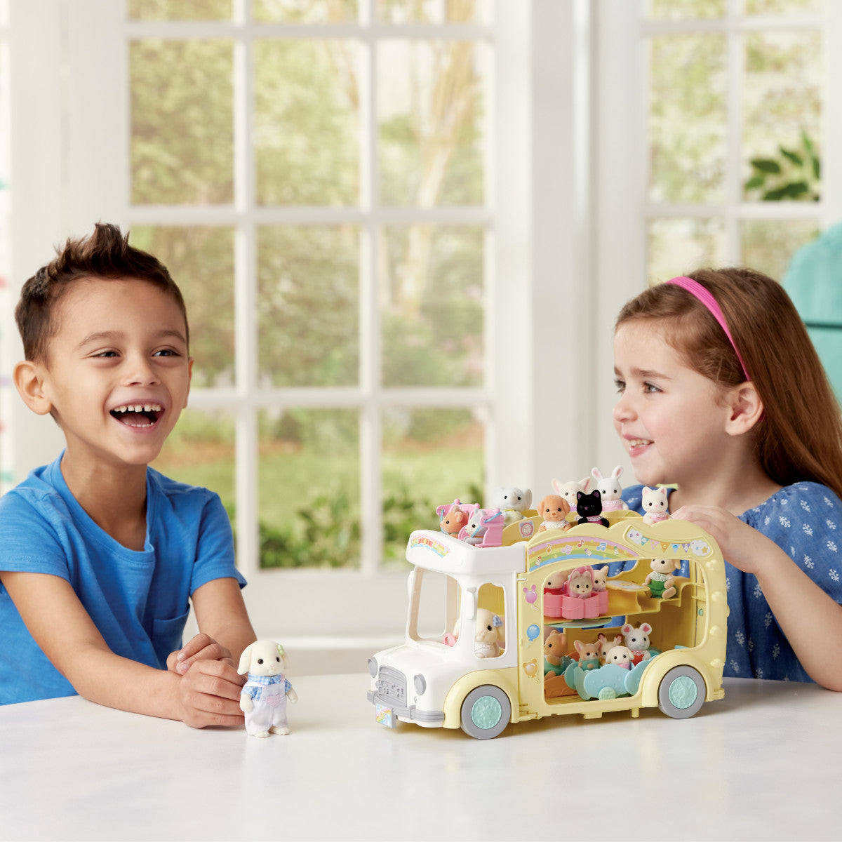 Two children happily playing with a colorful Rainbow Fun Nursery Bus toy filled with small animal figures indoors