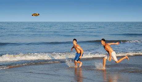 Two men playing on the beach throwing a MayaFlya Pocket Disc | Sports with waves in background.