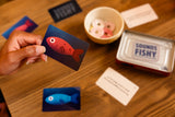 Sounds Fishy Travel Tin with colorful fish cards and game pieces on a wooden table