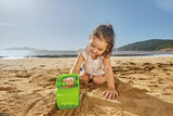 Little girl playing on sunny sandy beach using bright green toy shovel to dig in sand