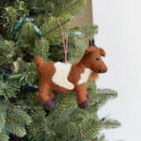 Handmade felt goat ornament in brown and white wool hanging on a Christmas tree branch with red string.