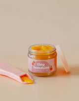 Small glass jar of peach jelly with a pink spoon holding jelly beside it on a beige background