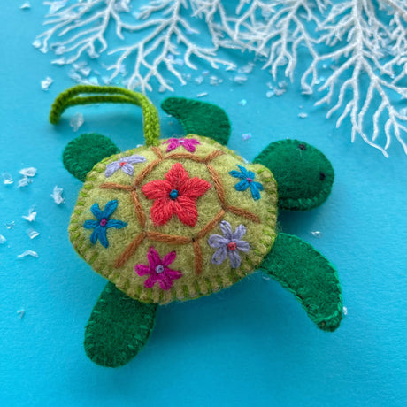 Green felt sea turtle ornament with colorful floral embroidery on its shell against a blue background