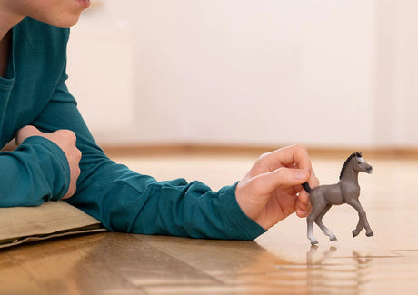 Person lying on the floor playing with a small Horse Cheval de Selle Francais Foal toy figurine.