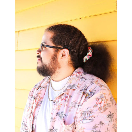 Man with curly hair wearing a Snail Mushroom Hair Scrunchie holding hair back against yellow wall background
