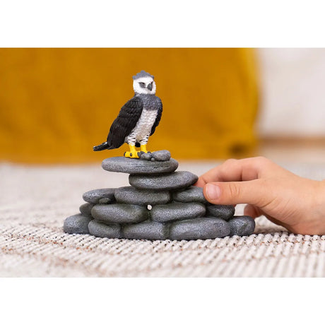 Harpy Eagle toy figure perched on stacked gray stones with a child's hand nearby for imaginative play.