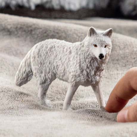 Arctic Wolf figurine with detailed white fur, showcasing its elegant build and size compared to a human finger.