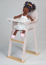 Wooden baby doll high chair with a white tray holding a doll wearing a white dress and pink shoes
