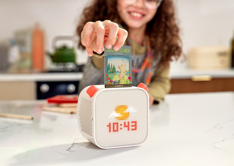 Person inserting a colorful card into a small white digital clock on a kitchen counter