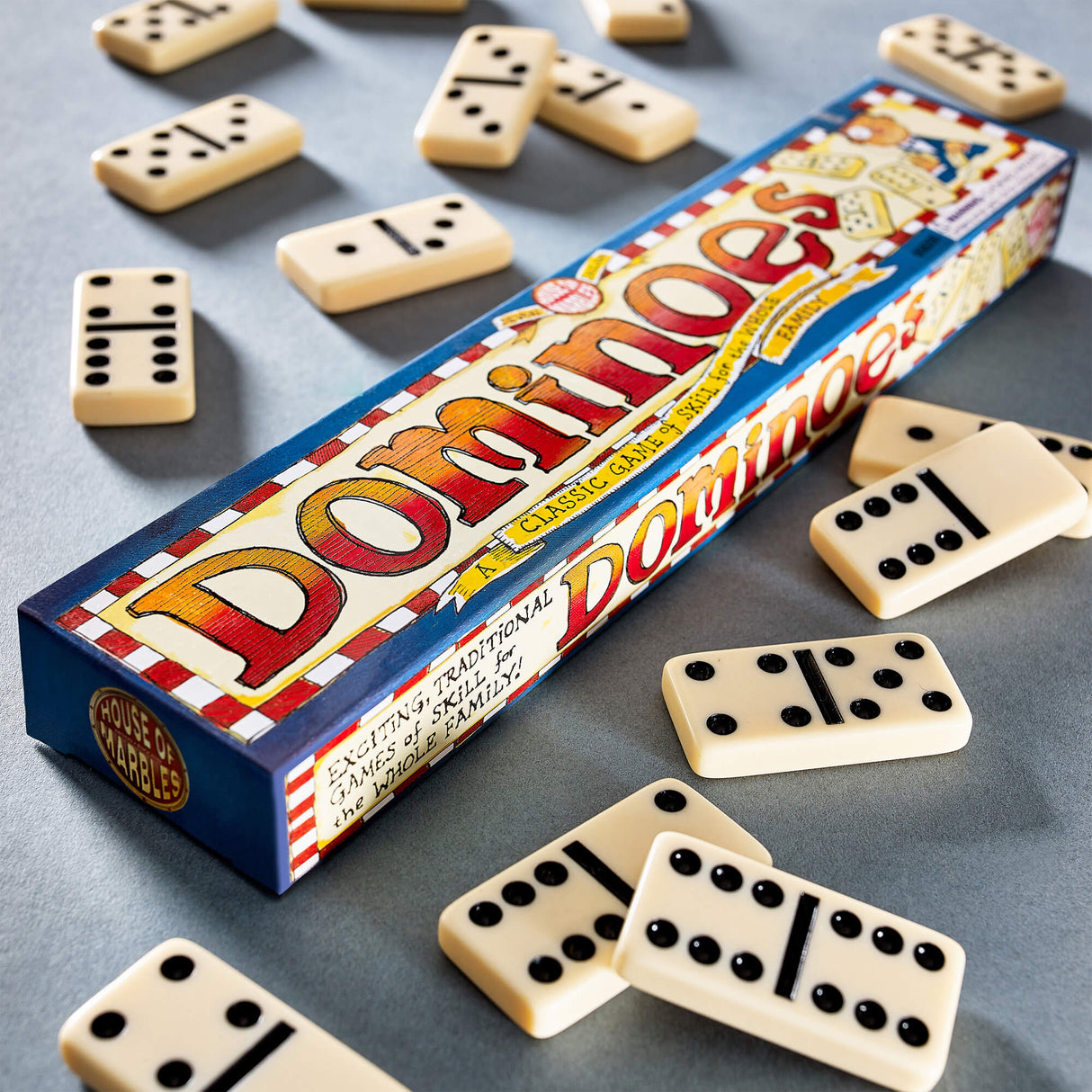 Classic dominoes set with black dots scattered around colorful rectangular box on gray surface