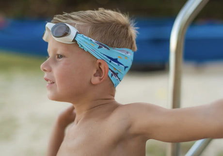 Child wearing Googles Shark Attack swim goggles with shark print strap and white frame by the pool.