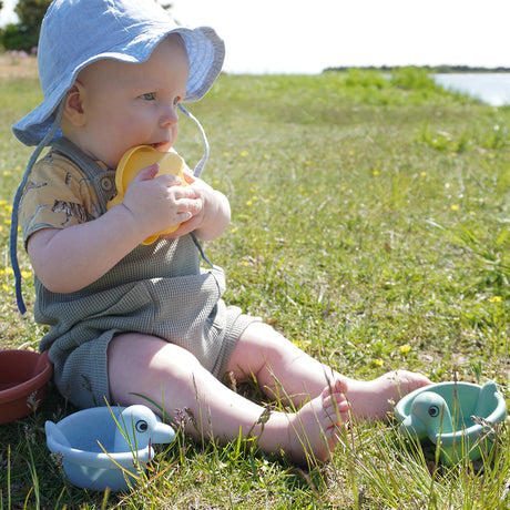 Baby playing outdoors with colorful Re:line Bath Ducks made from 100% recycled plastic in a sunny grassy area.