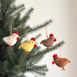 Four colorful felt chicken ornaments hanging on a pine tree branch for festive holiday decor