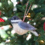 Handmade felt wool bird ornament in gray and cream hanging on a Christmas tree branch with lights nearby