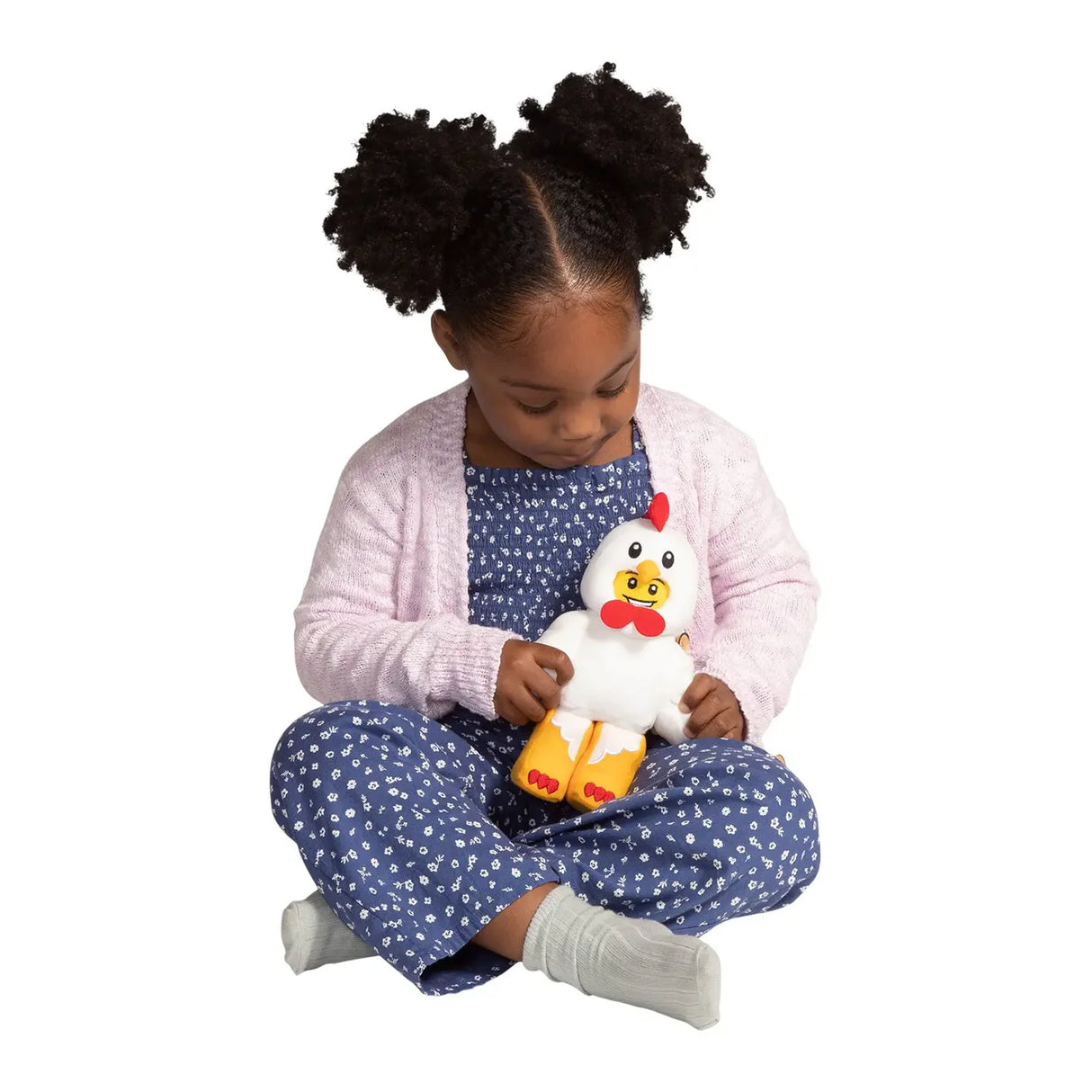 Young girl in blue floral outfit and pink cardigan sitting cross-legged holding a white plush chicken toy