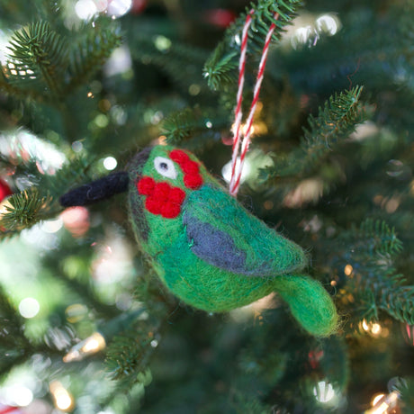 Handmade felt wool bird ornament in green with red and black details hanging on a Christmas tree branch