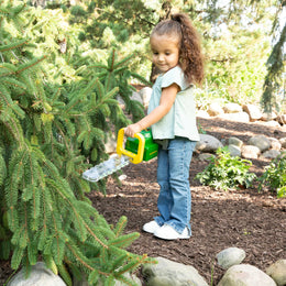 Child watering a young evergreen tree with a green and yellow watering can in a garden