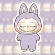 Closed-eyed Labubu character in a pastel purple onesie with bunny ears, smiling softly on a vinyl sticker.