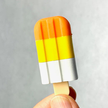 Hand holding a Japanese Eraser Ice Cream shaped like a colorful popsicle with orange, yellow, and white sections.