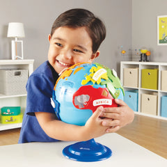 Young boy in blue shirt hugging colorful globe toy with labeled continents and animals at white table