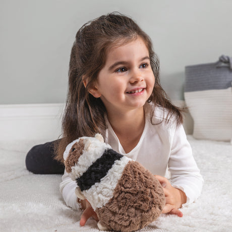 Child lying on carpet playing with soft plush Putty Guinea Pig Gizmo toy in muted neutral colors.