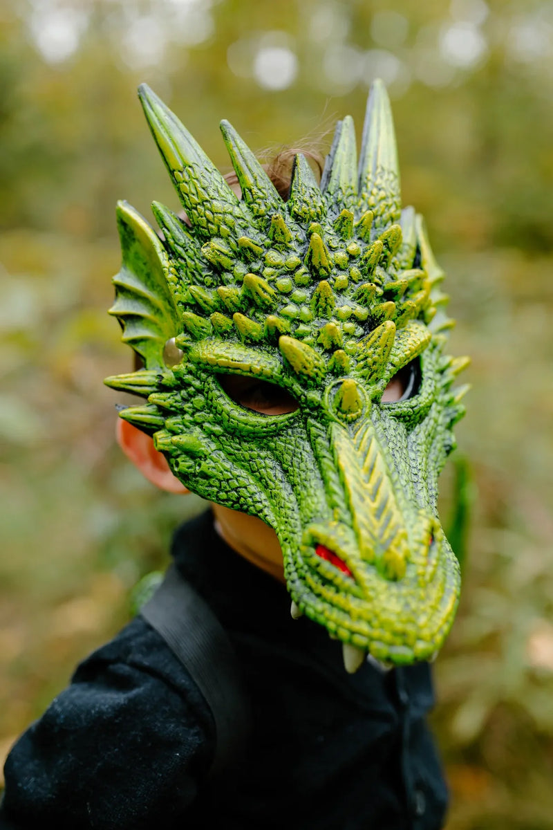 Person wearing a detailed green dragon mask outdoors among blurred trees