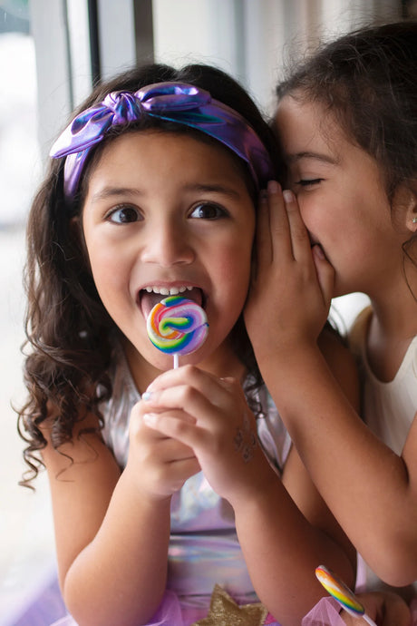 Two young girls smiling, one wearing a Midnight Metallic Headband with purple-blue metallic shine and bow detail.