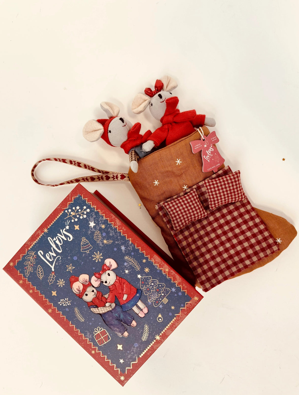 Two festive mice dolls dressed in holiday outfits inside a brown and red checkered Christmas stocking with a gift box nearby