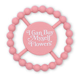 Round pink teething toy with raised beads and "I Can Buy Myself Flowers" text in white letters