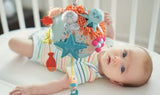 Baby lying in crib reaching for Sensorial Reef soft coral and octopus-shaped rattle toy for sensory play and learning.