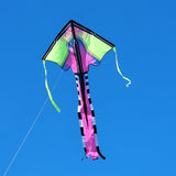 Diamond-shaped kite in neon green and pink with black and white striped tail flying against clear blue sky