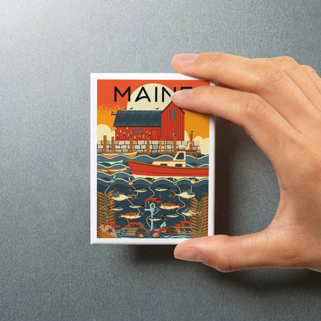 Hand holding a Maine Nautical Geometric Magnet featuring a colorful coastal scene with a boat and fish on a silver background.