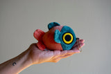 Hand holding a soft, round mochi fish fry plush keychain with vibrant blue and orange colors and a small chain attached