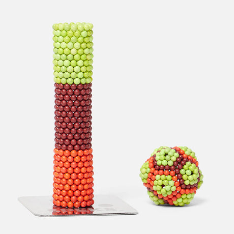 Speks. Bolds. Brash colorful magnetic balls stacked in a tower and shaped into a sphere on a white surface.