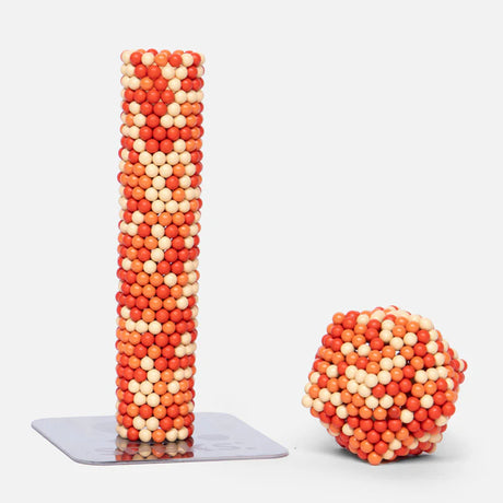Speks. Pixel. 1 Up. shows colorful magnetic balls formed into a tall tower and a compact sphere on a white surface.