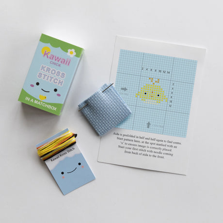 Kawaii Chick Mini Cross Stitch Matchbook with blue Aida cloth, yellow thread, needle, and cute chick pattern instructions.