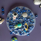 Round sensory pad filled with blue beads and space-themed charms including astronaut, planet, and moon designs