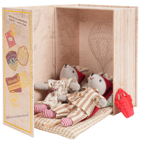 Two sleepy mice dolls dressed in pajamas resting inside a cozy book-shaped box with travel-themed designs