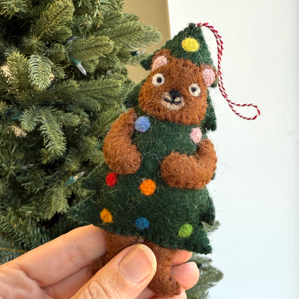 Handmade felt ornament of a brown bear dressed as a Christmas tree with colorful wool decorations hanging by loop