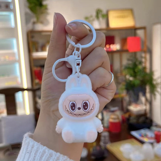 Close-up of hand holding a cute white Labubu Flocking Keychain with big eyes and bunny ears in cozy setting.