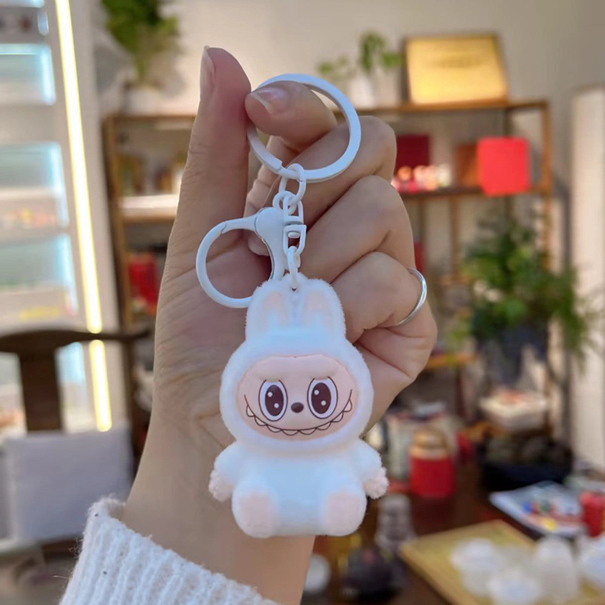 Hand holding Labubu Flocking Keychain with fuzzy texture and playful face in cozy indoor setting.