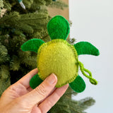 Handmade green felt sea turtle ornament with detailed stitching held in front of a Christmas tree background