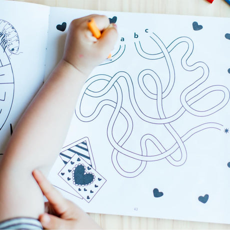 Child tracing a heart-themed maze with an orange marker to develop problem-solving skills and hand-eye coordination