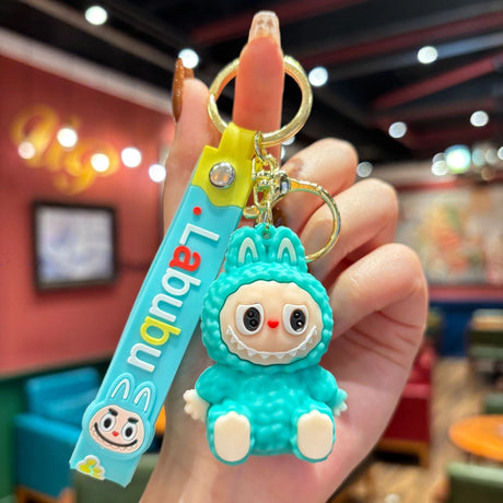 Hand holding Labubu Silicone Keychain featuring a cute turquoise character and colorful strap in a cozy indoor setting.
