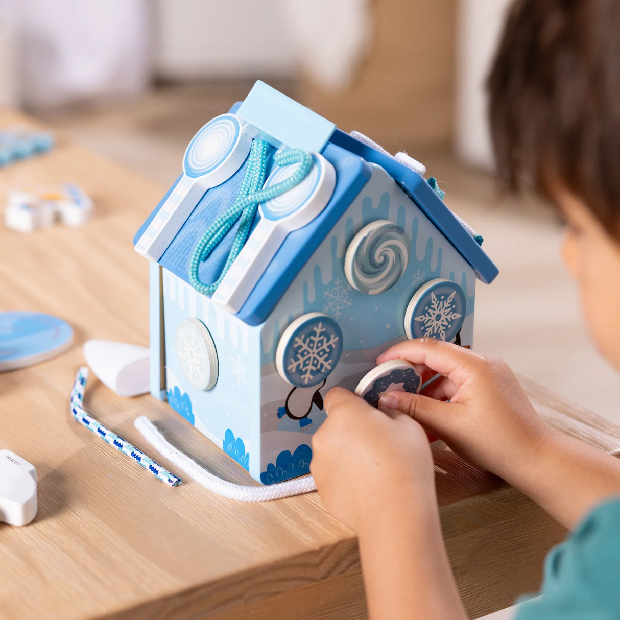 Child playing with a blue wooden gingerbread house featuring reusable decorative accessories and icing cords for creative play.