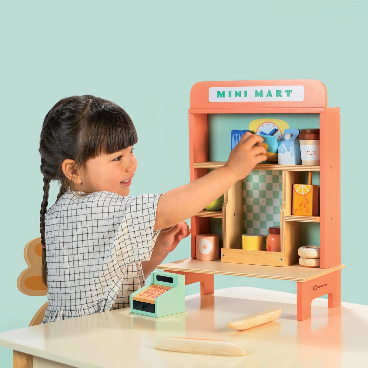 Young girl playing with a retro-style Mini Mart playset featuring shelves stocked with miniature groceries and a small till