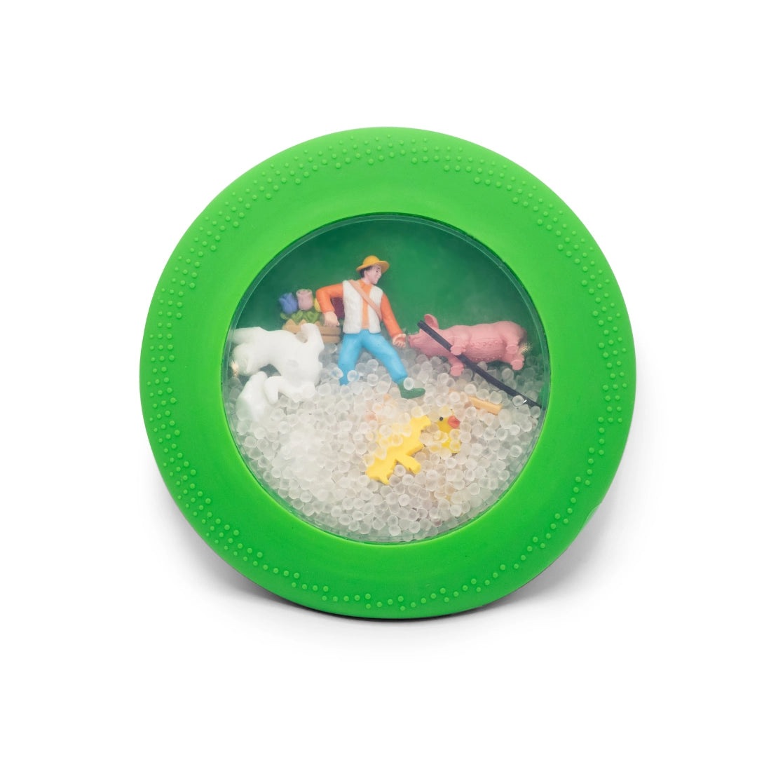 Round green sensory toy with clear center containing farm animal figurines, a farmer, and small translucent beads inside