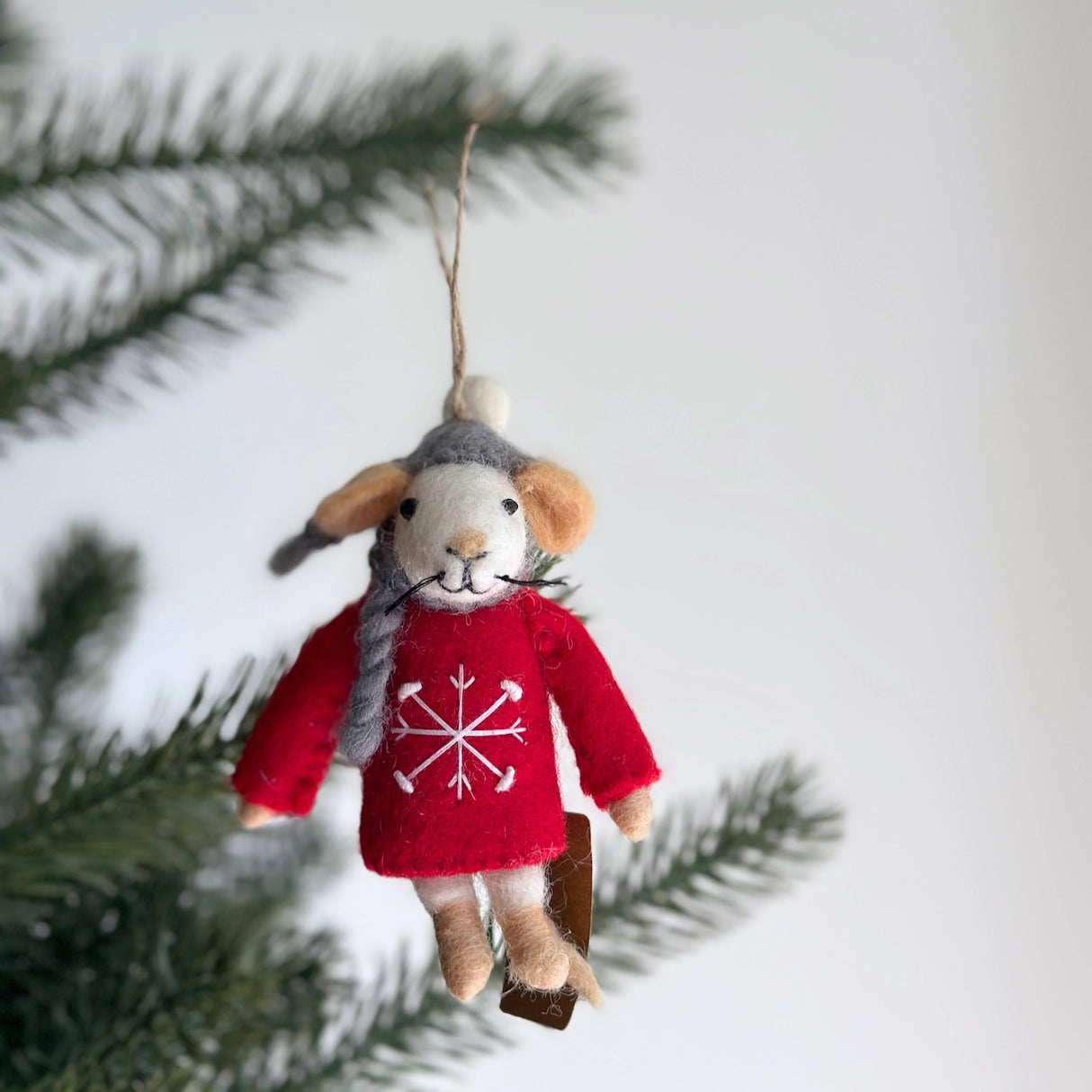 Handmade felt mouse ornament wearing a red sweater with snowflake and a gray winter hat hanging on a tree branch